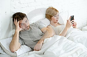 Couple in bed husband frustrated upset unsatisfied while wife using mobile phone