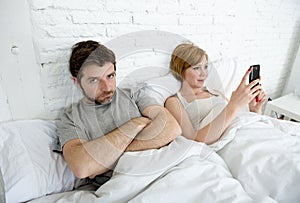 couple in bed husband frustrated upset unsatisfied while wife using mobile phone