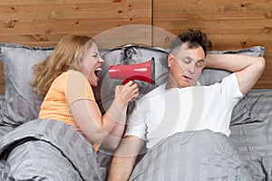 Couple in bed, man sleeping and snoring, disgruntled woman yelling at him in red megaphone. Snoring as a problem