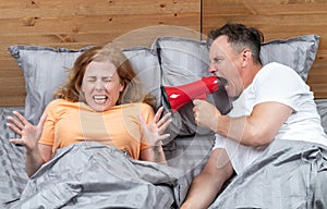 Couple in bed, a man yells at a frightened woman through a red megaphone. Clarification of relations