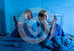 Couple in bed on mobile phones ignoring each other in relationship problems and technology addiction