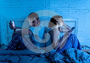 Couple in bed on mobile phones ignoring each other in relationship problems and technology addiction