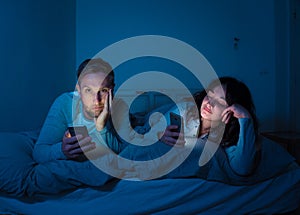 Couple in bed on smart phones ignoring each other in relationship problems and technology addiction