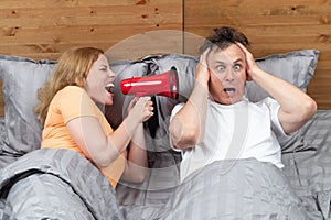 Couple in bed, a woman shouts into a red megaphone at a man who wakes up with fright in his eyes. Snoring as a problem