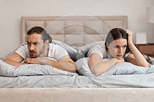 Couple in bed with worried expressions facing away