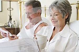 Couple in bedroom with coffee and newspapers