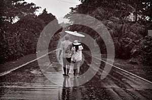 Couple from behind walking on the road on a rainy day with palm trees on both sides