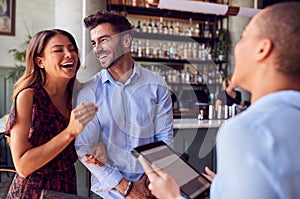 Couple Being Greeted By Maitre D Using Digital Tablet As They Arrive At Restaurant