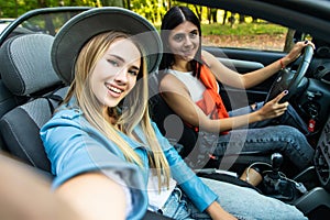 Couple of best friends women taking a selfie at car trip. Two young girl having fun togheter smiling at the camera