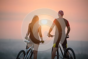 Couple bicyclist with mountain bikes on the hill at sunset