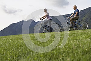 Couple Biking On Grass Against Mountain Range