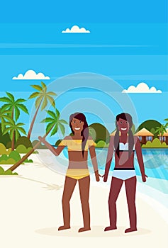 Couple bikini women on tropical island with villa bungalow hotel on beach seaside green palms landscape summer vacation