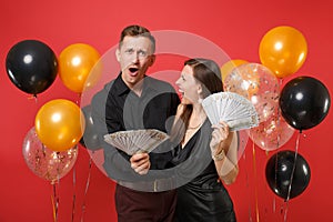 Couple in black clothes celebrating birthday holiday party hold lot cash money on bright red background air