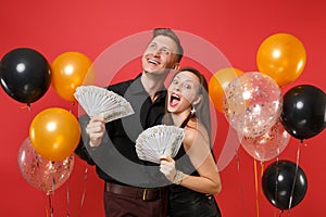 Couple in black clothes celebrating birthday holiday party hold lot cash money on bright red background air