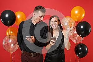 Couple in black clothes messaging in cellphone celebrating birthday holiday party isolated on red background air