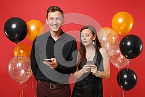 Couple in black clothes messaging in cellphone celebrating birthday holiday party isolated on red background air