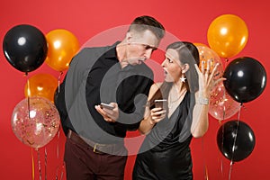 Couple in black clothes messaging in cellphone celebrating birthday holiday party on red background air