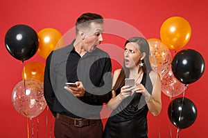 Couple in black clothes messaging in cellphone celebrating birthday holiday party on red background air