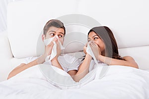 Couple blowing their noses at home