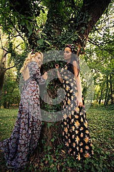 Couple of boho style women stand by huge tree in wood