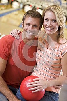 Couple in bowling alley holding ball and smiling