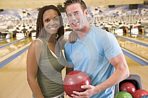 Couple in bowling alley holding ball and smiling