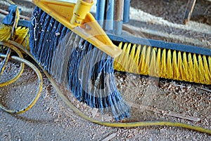 A couple of brooms and a dirty floor of a workshop.