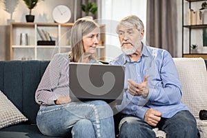Couple browsing webstore via laptops while sitting on couch