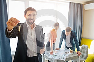 Couple buy or rent apartment together. They stand at table behind and look down on plans. Young realtor in front smile