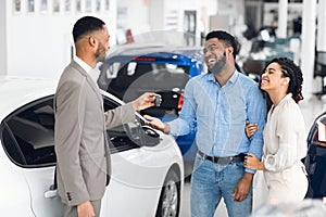 Couple Buying Car Taking Key From Salesman In Auto Showroom