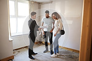 Couple Buying House For The First Time Looking At Survey With Realtor