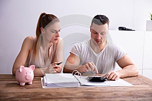 Couple Calculating Bills Using Calculator Near Piggy Bank