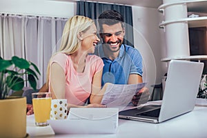 Couple calculating budget at home. Smiling woman and man looking at laptop screen, checking finances, sitting at table at