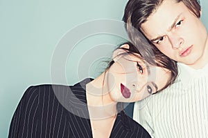 Couple on calm faces dressed in fashionable clothes. Girl with make up lean on male shoulder, grey background. Fashion