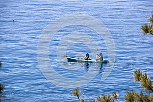 Couple in canoe on very blue textured water framed with pine braches - muscled man rowing while woman enjoys ride - Lake Tahoe