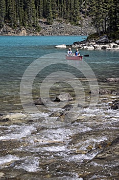 Couple canoeing in front of turbulent river entering glacial lake Moraine in Banff National Park, Alberta, Canada