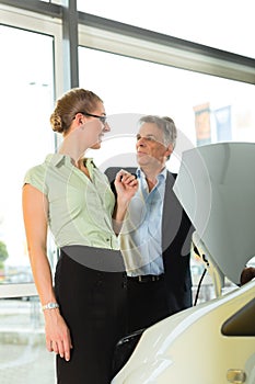 Couple in car dealership looking under a hood