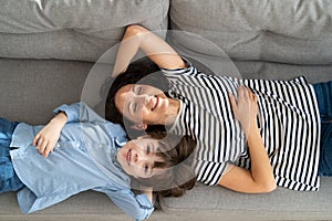 Couple of carefree mother and cute child lying, resting on couch having fun looks together at camera