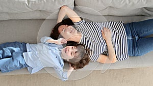 Couple of carefree mother and cute child lying, resting on couch having fun looks together at camera