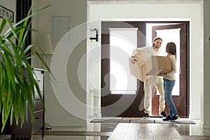 Couple carrying boxes entering house, homeowners moving in new h