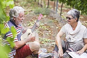 Couple of caucasian adult senior stay together outdoor in leisure activity playing an ukulele guitar doing serenade for the lady.