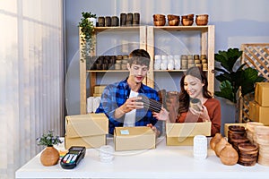 Couple of Caucasian male and Asian female sell vase products online live streaming at home. Packing vase parcels for send by order