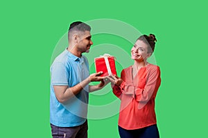 Couple celebrating Valentines day. Young handsome man in casual clothes giving box to beautiful elegant woman. isolated on green photo