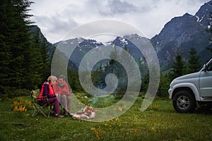 Couple chatting by bonfire in a camping in a dark mountain valley. White car.