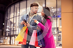 couple checks phone for sales shopping during winter spree outdoor