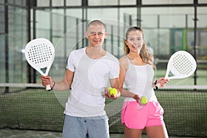 Couple of cheerful young paddle tennis players standing on indoor court