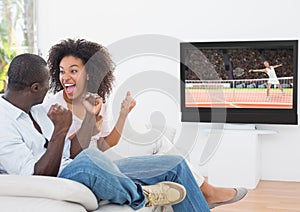 Couple cheering while watching tennis match on television