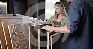 Couple choosing wood texture laminate floor from samples for home improvements in interior design store