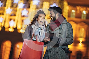 Couple in the city centre with holiday`s brights in background. Couple browsing digital tablet. They are using credit card