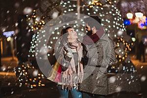 Couple in the city centre with holiday`s brights in background. Couple holding gift in a Christmas night